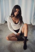 Woman wearing Studio Élancé Pilates grip socks, long sleeve top, and shorts, seated on studio floor